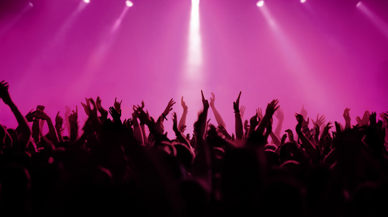 Hands raised at a concert under pink lights