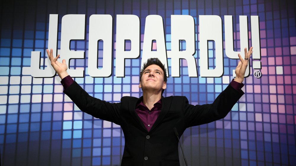 A photograph of James Holzhauer in front of the Jeopardy! logo.