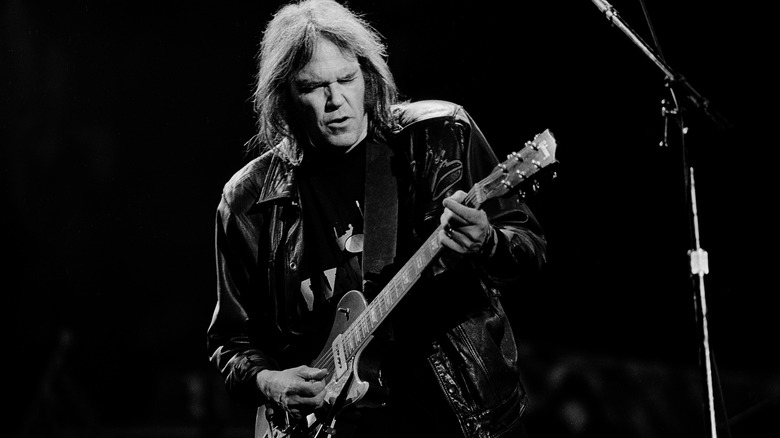 Neil Young singing and playing guitar onstage with eyes closed