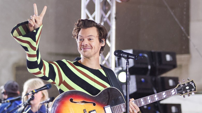 Harry Styles with guitar smiling giving peace sign