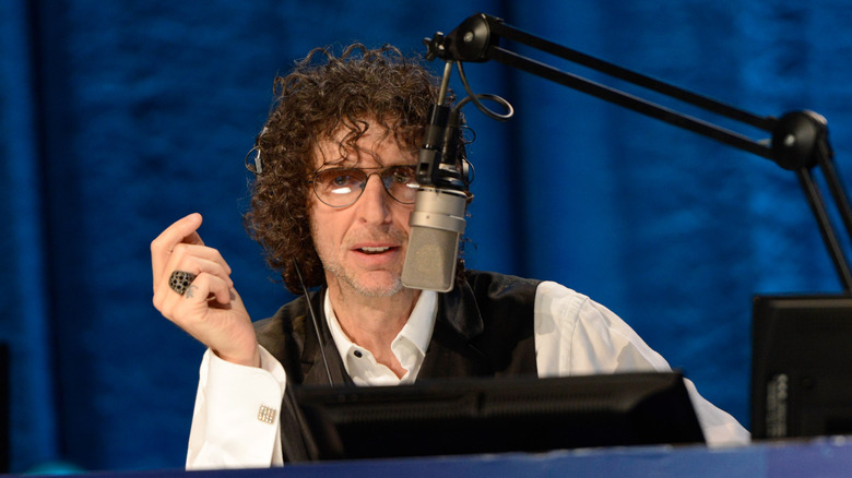 Howard Stern at microphone with hand raised