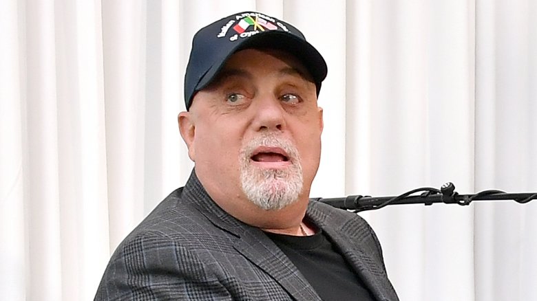 Billy Joel cap and suit sat looking to side mouth open