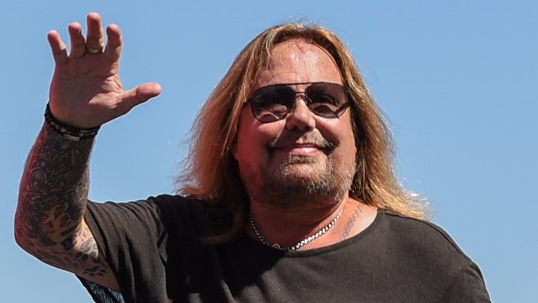 Vince Neil long hair and sunglasses waving and smiling outside