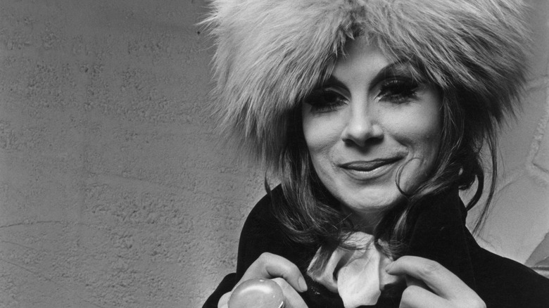 April Ashley fluffy wig holding jacket smiling