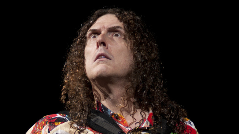 Weird Al Yankovic looks up with mock seriousness while playing accordion on stage.