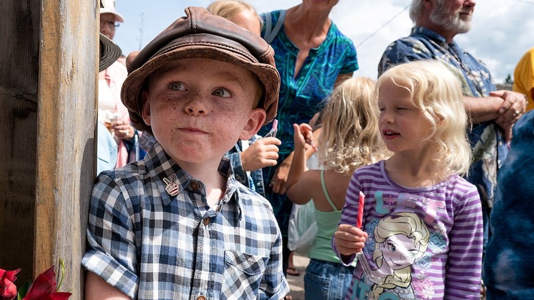 Boy in flat cap and girl eating candy outside with adults