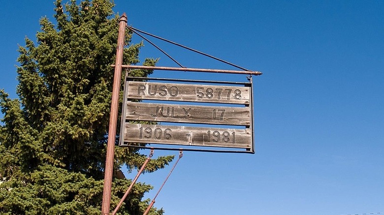 Wooden sign for Ruso with population by tree sunny