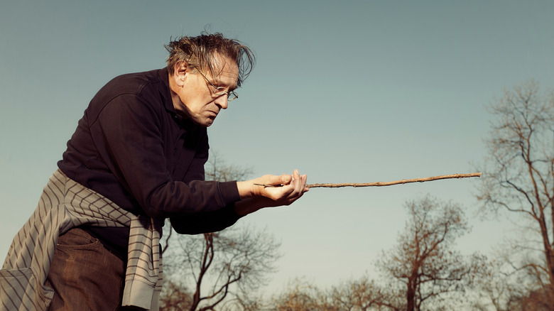 man black shirt glasses holding stick dowsing rod