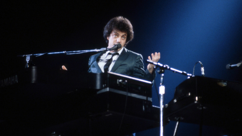 Billy Joel at his piano speaking into a microphone onstage