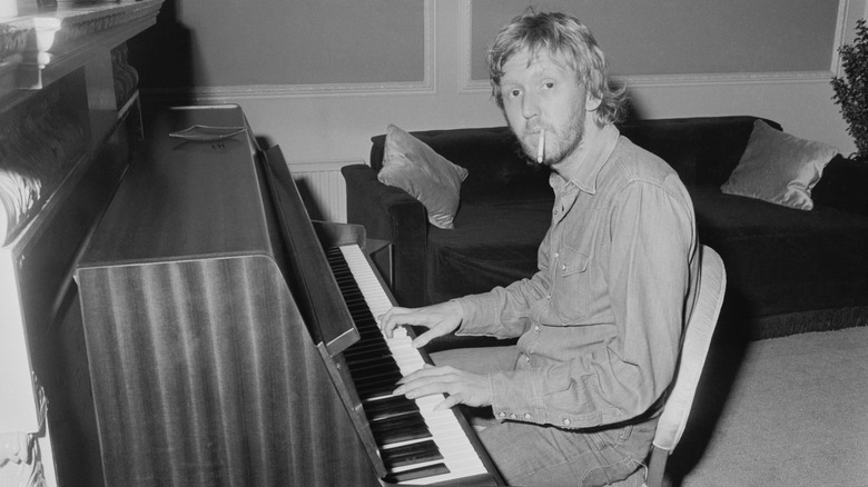 Harry Nilsson seated at a piano smoking a cigarette