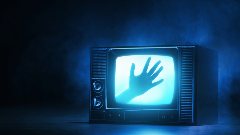 Hand silhouette seen on vintage TV, dark background and blue smoke effects