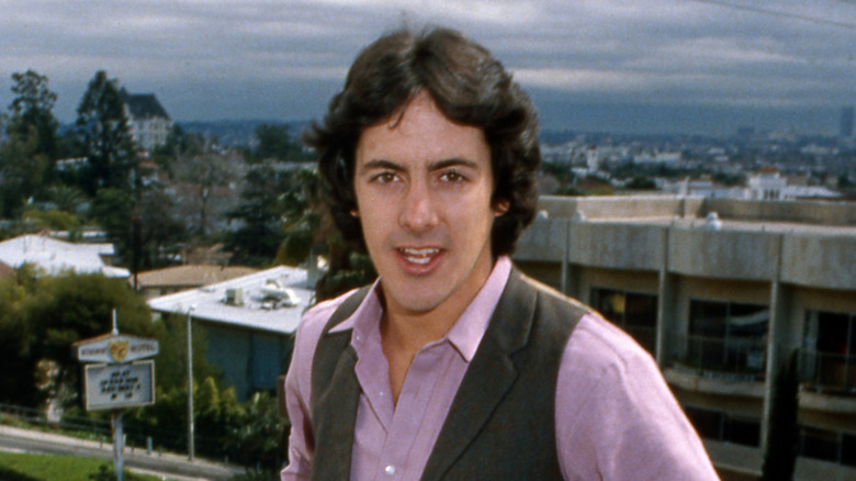 David Naughton smiling in pink shirt with city in background