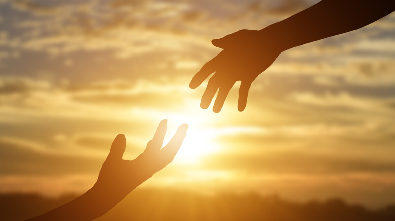Hands reaching out silhouetted against sun