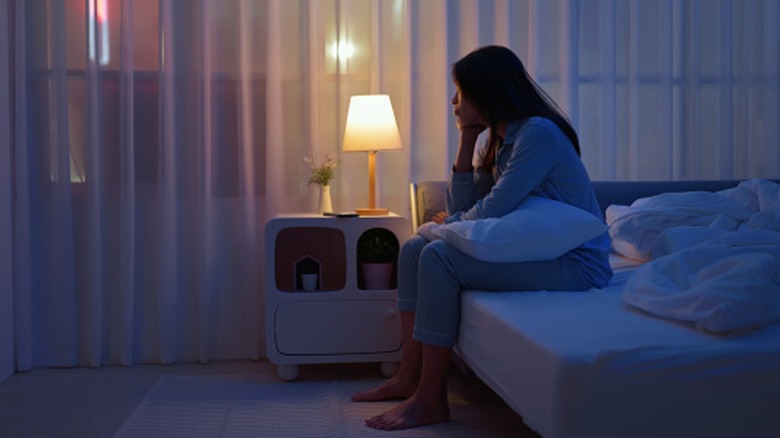 Woman sits on side of bed with head in chin