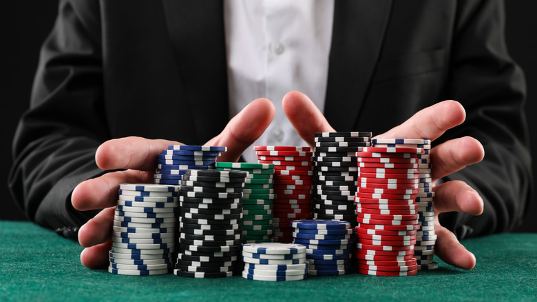 Closeup of hands pushing large stack of casino chips forward.