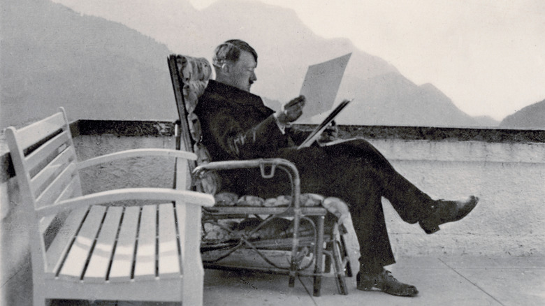 Hitler reading files while sitting outdoors in chair.