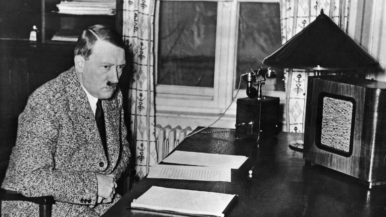 Hitler sitting at desk, listening to large radio.