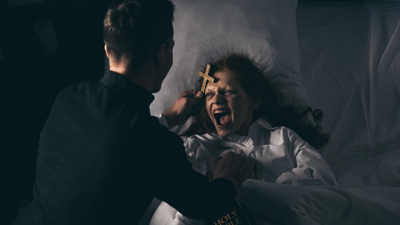 Exorcist with bible and cross over girl in bed