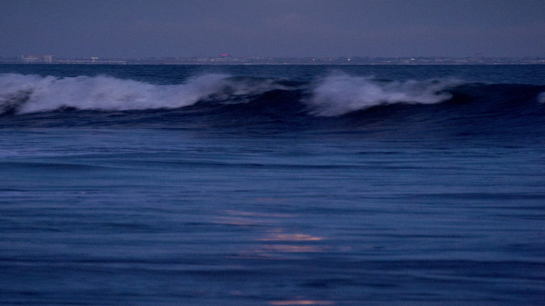 the moon hanging over a city and crashing waves
