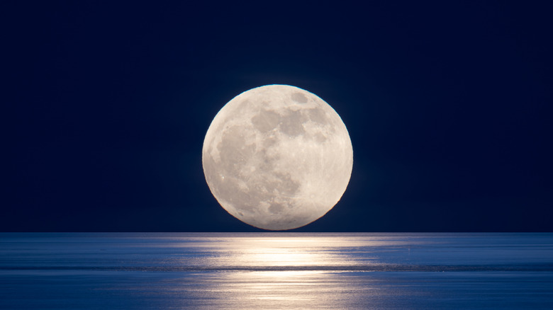 full moon setting over calm ocean