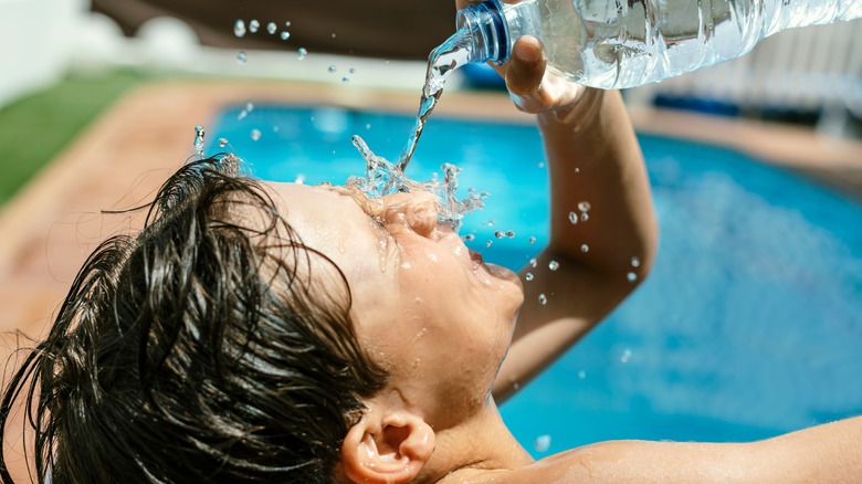 Kid in pool pouring water bottle