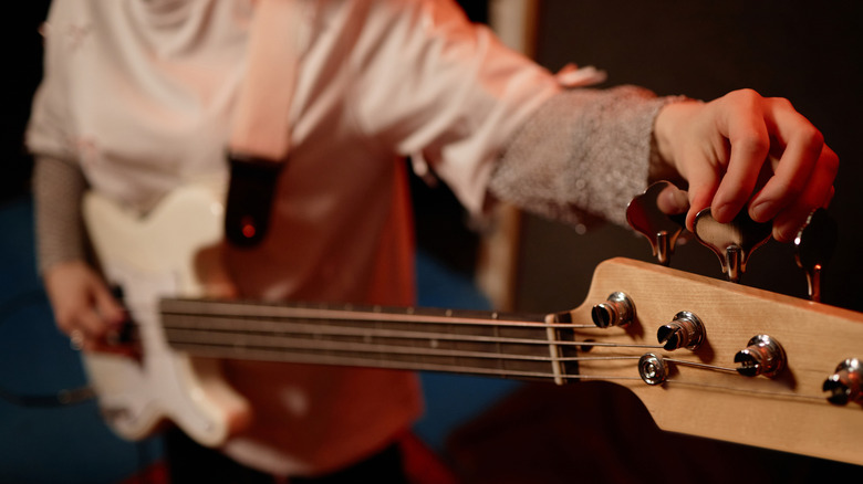 A musician adjusting bass guitar strings.