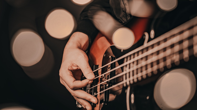 Close-up of person plucking strings on bass guitar.
