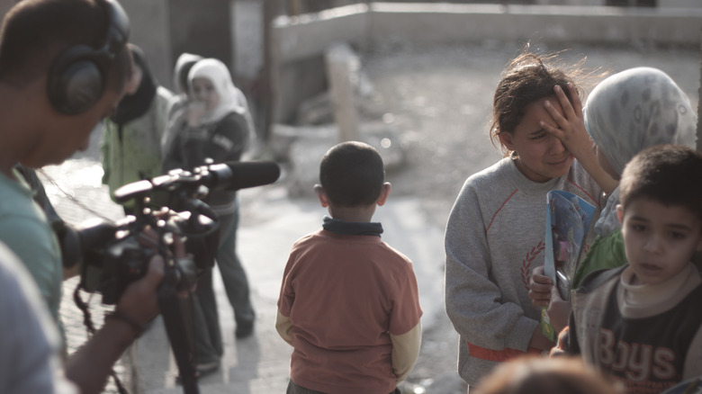 Syrian refugee kid crying whilst a media reporter is recording the moment