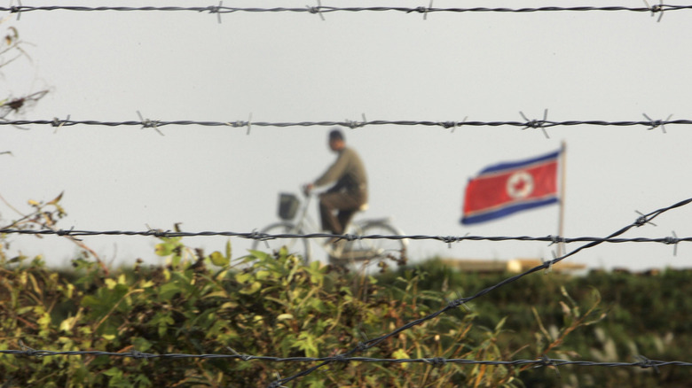 North Korean man riding a bicycle near a North Korean flag seen through the fence on Chinese side, 2006.