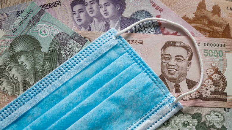 Blue medical face mask laid against North Korean paper money.