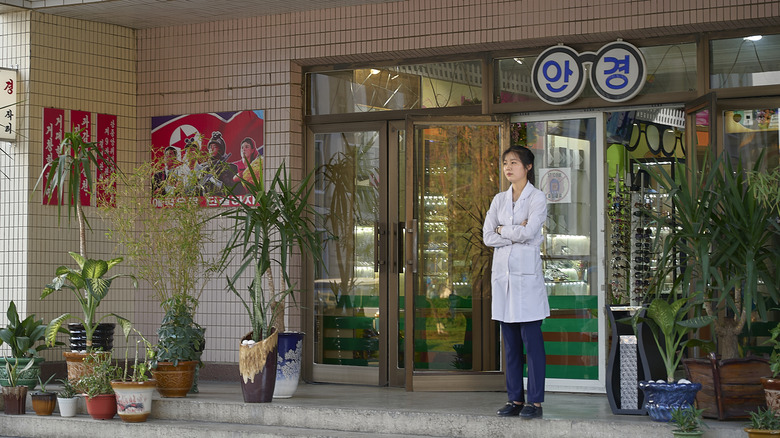 A female store clerk standing outside shop in Pyongyang, North Korea.