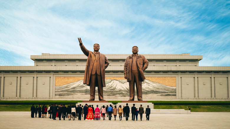 Side by side statues of Kim Jong Un in North Korea, with citizens looking on from the ground.