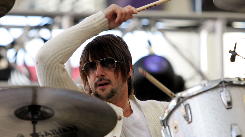 Jason Sutter playing drums in white sweater and sunglasses