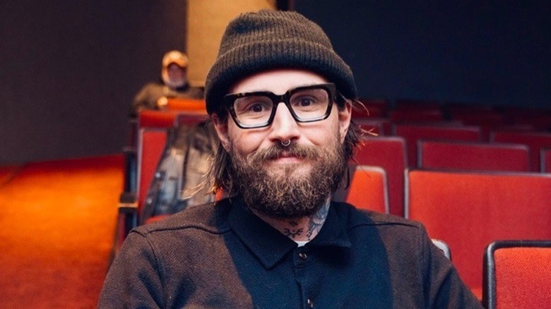 Spencer Rollins sitting down and smiling in glasses, beard, and beanie hat