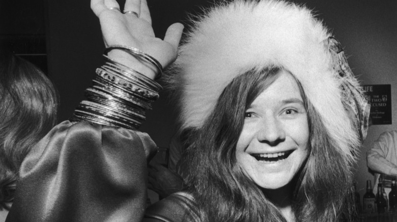 Janis Joplin smiling and waving in a furry hat