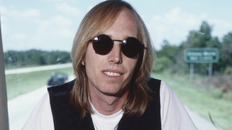 Tom Petty smiles in a bus while wearing sunglasses