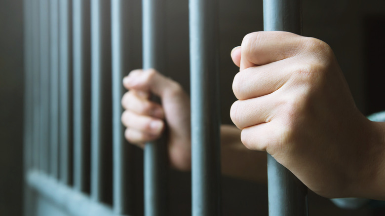 hands holding bars of a jail cell