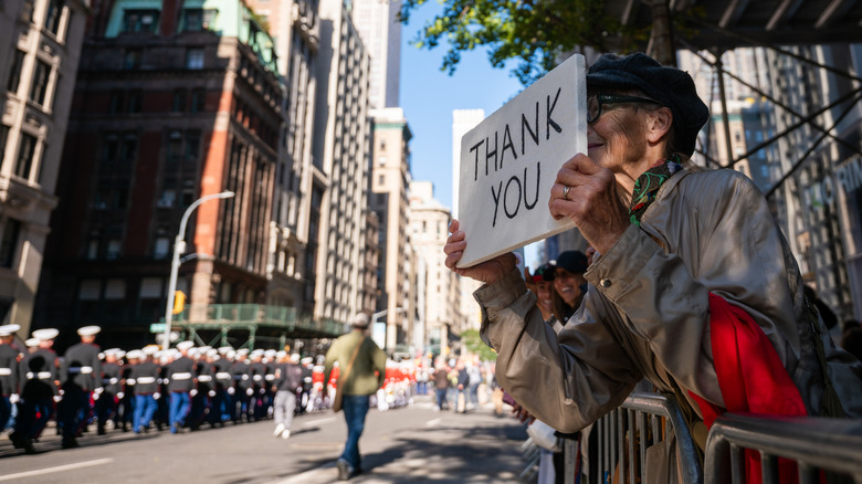 Woman holding a "thank you" sign to military members during a Veterans Day parade