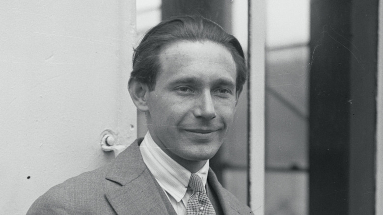 Jean Borotra in suit and jacket grinning and looking away