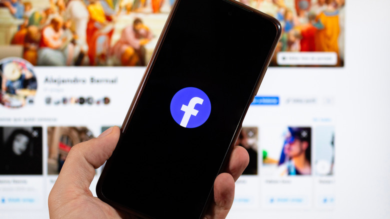 hand holding phone with Facebook logo