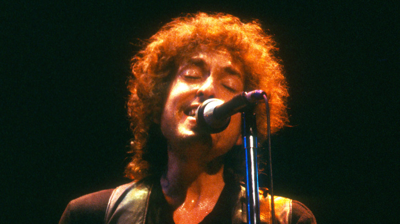 Bob Dylan singing into mic on stage with long curly hair