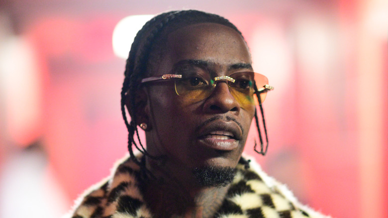 Rich Homie Quan in yellow shades and checkered fur coat looking away