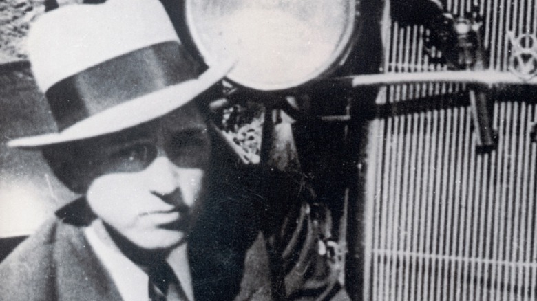 Clyde Barrow kneels in front of his car