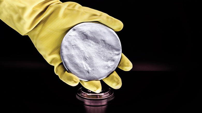 gloved hand holding a radioactive metal disk on a black background