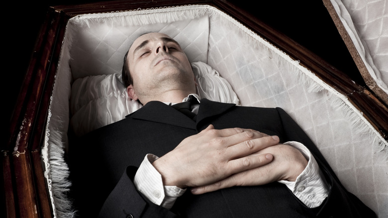 Person lying in a casket with hands on abdomen