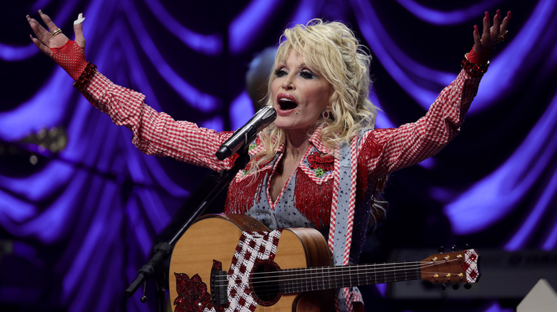 Dolly Parton singing on stage with hands raised