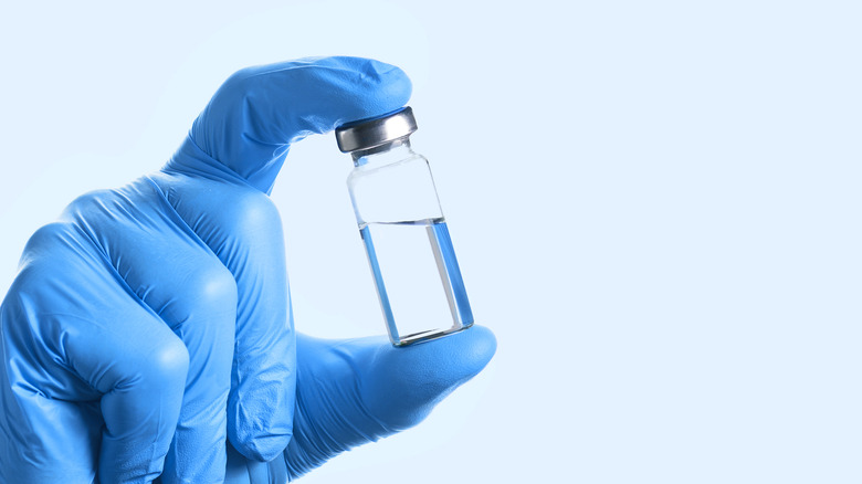 gloved hand holding vial of drug