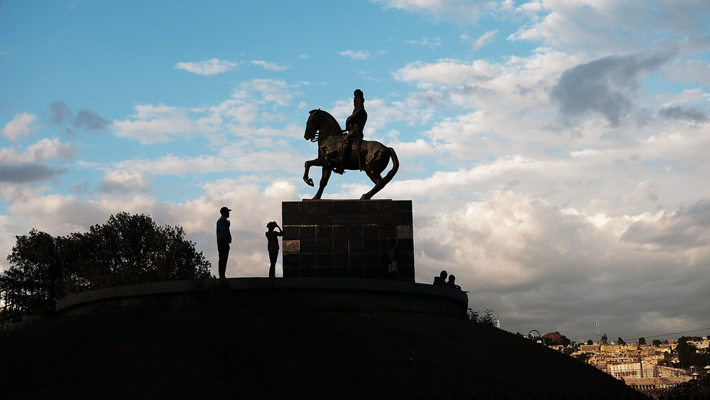 People stand under a statue of Jean-Jacques Dessalines, a leader of the Haitian Revolution and the first ruler of an independent Haiti, in Port au Prince on February 10, 2018 in Port-au-Prince, Haiti.