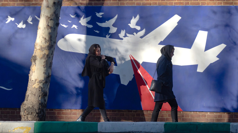 women walk past a memorial mural to iran air flight 655