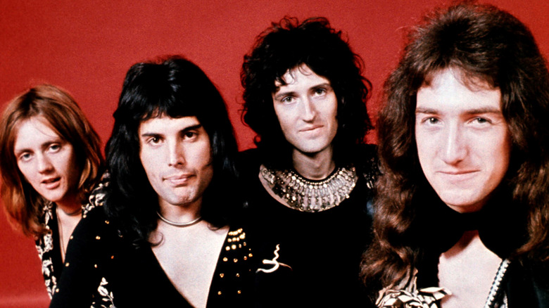 Members of Queen posing in front of a red background